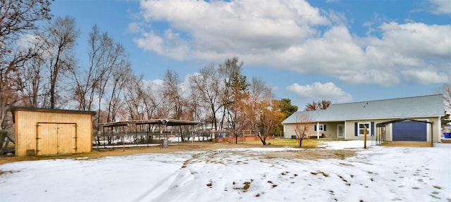 yard layered in snow featuring a shed, a carport, and a garage