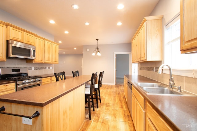 kitchen featuring appliances with stainless steel finishes, sink, a center island, a kitchen breakfast bar, and decorative light fixtures