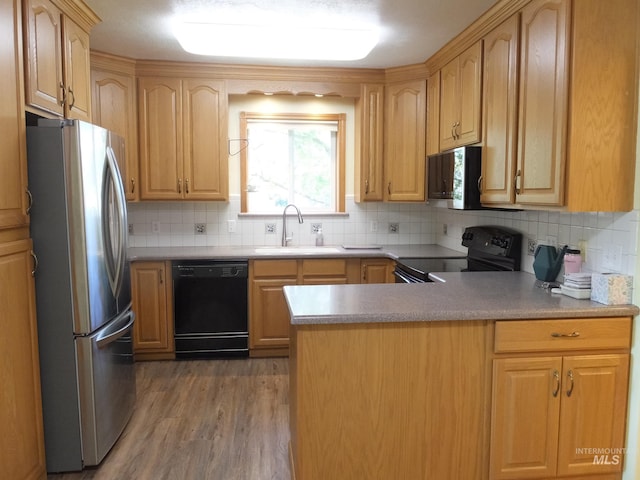 kitchen with a peninsula, wood finished floors, tasteful backsplash, a sink, and black appliances