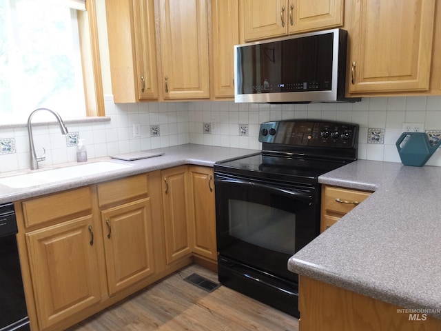 kitchen with visible vents, decorative backsplash, a sink, light wood finished floors, and black appliances