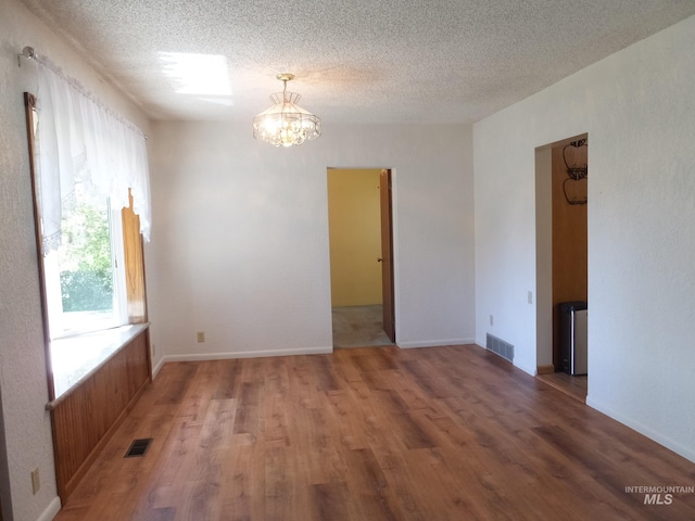 empty room featuring a notable chandelier, light wood-type flooring, and visible vents