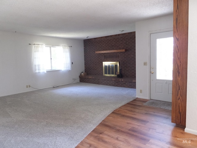 unfurnished living room featuring a healthy amount of sunlight, a textured ceiling, a brick fireplace, and wood finished floors