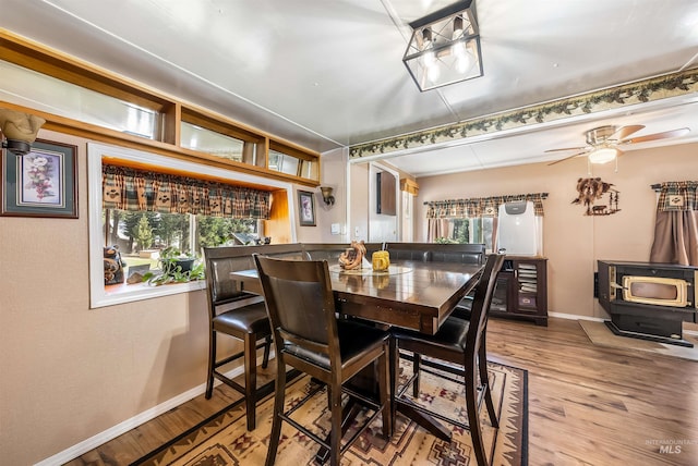 dining space with ceiling fan, a healthy amount of sunlight, hardwood / wood-style floors, and a wood stove