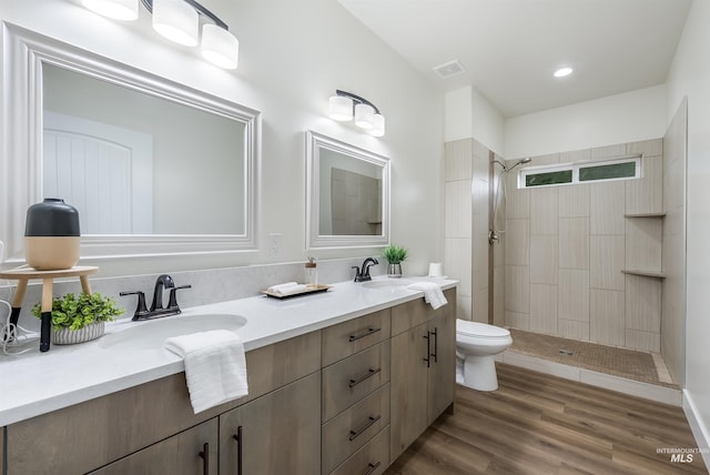 full bathroom with toilet, tiled shower, a sink, and wood finished floors