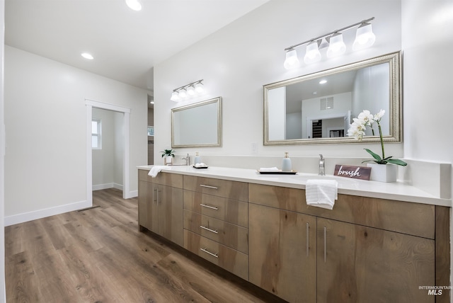 full bathroom featuring double vanity, visible vents, a sink, wood finished floors, and baseboards