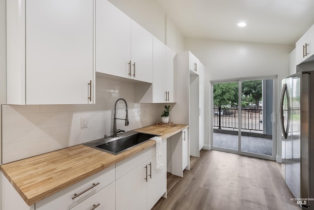 kitchen featuring a sink, white cabinetry, backsplash, freestanding refrigerator, and light wood finished floors