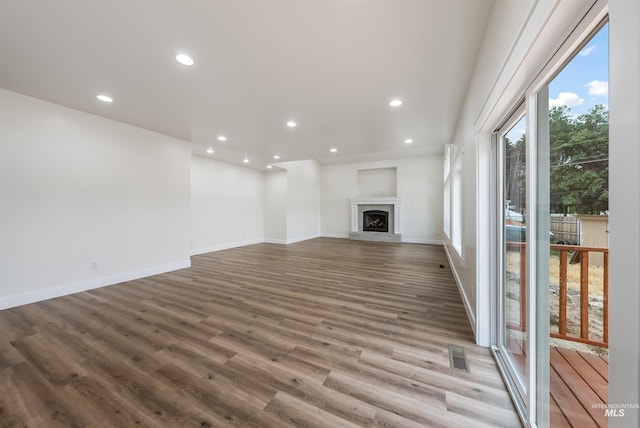 unfurnished living room featuring recessed lighting, visible vents, a fireplace with raised hearth, wood finished floors, and baseboards