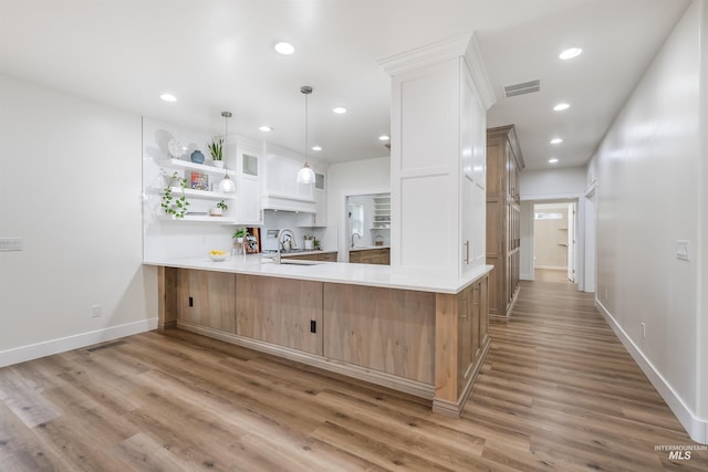 kitchen featuring light wood finished floors, white cabinets, a peninsula, light countertops, and open shelves