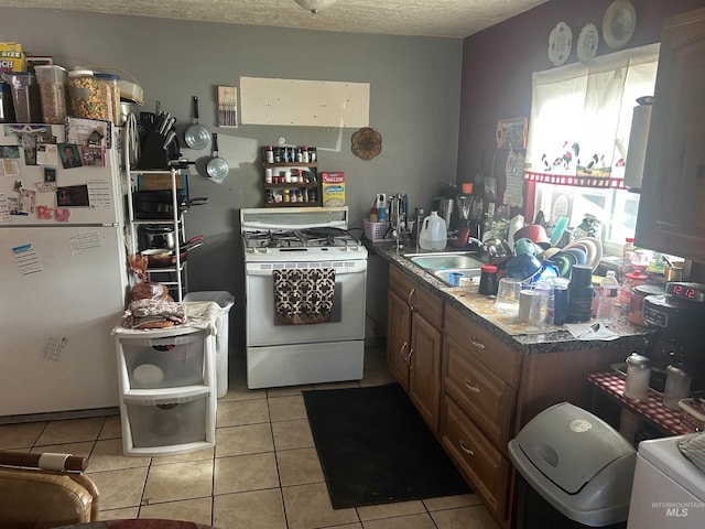 kitchen with light tile patterned floors, brown cabinets, white appliances, a textured ceiling, and a sink