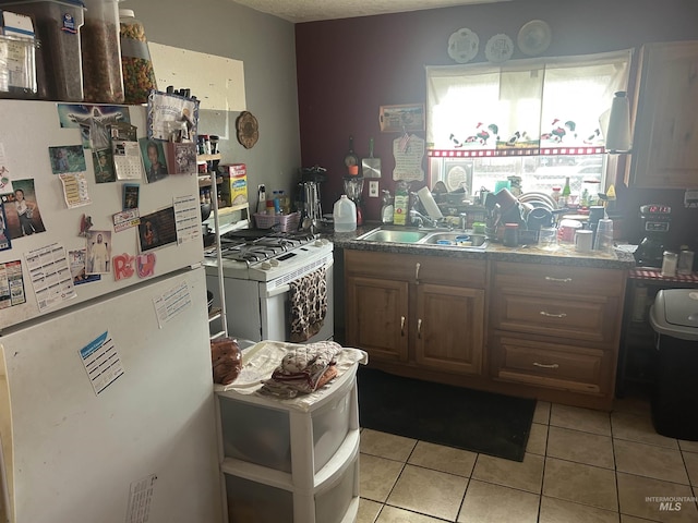 kitchen with light tile patterned flooring, white appliances, and a sink