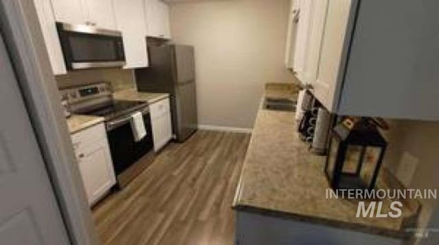 kitchen with light stone counters, white cabinets, stainless steel appliances, dark hardwood / wood-style floors, and sink