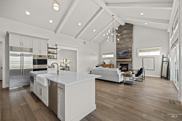 kitchen featuring sink, a fireplace, high vaulted ceiling, an island with sink, and stainless steel appliances