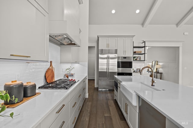 kitchen with beamed ceiling, appliances with stainless steel finishes, premium range hood, sink, and dark hardwood / wood-style floors