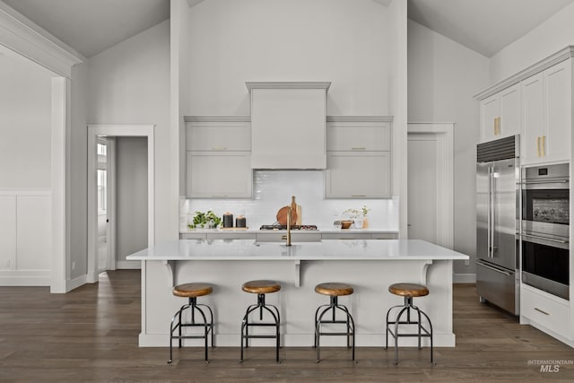 kitchen with wall chimney exhaust hood, a kitchen bar, a kitchen island with sink, and stainless steel appliances