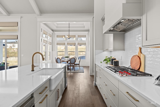 kitchen featuring pendant lighting, tasteful backsplash, sink, stainless steel gas stovetop, and custom range hood