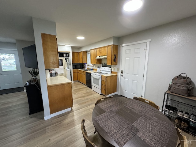 kitchen featuring brown cabinets, light countertops, black appliances, under cabinet range hood, and light wood-style flooring