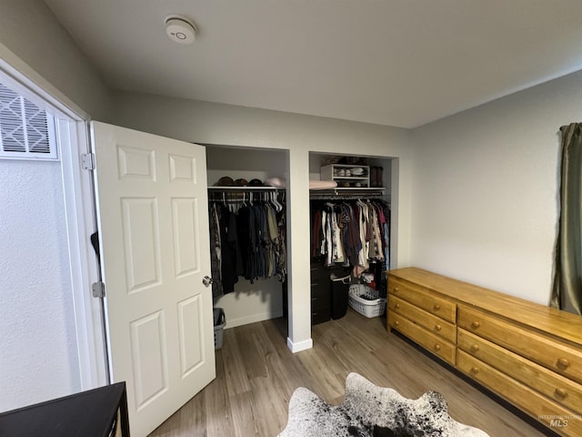 bedroom with wood finished floors, baseboards, and two closets