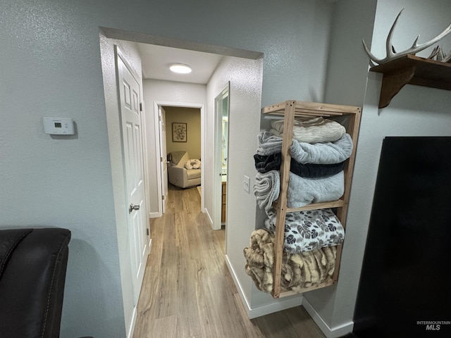 hallway featuring baseboards, a textured wall, and wood finished floors
