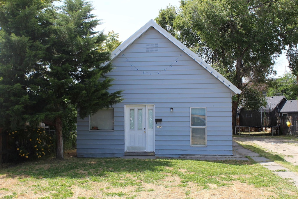 rear view of property featuring a trampoline and a lawn