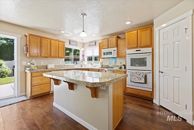 kitchen with white appliances, light countertops, dark wood-type flooring, and a center island