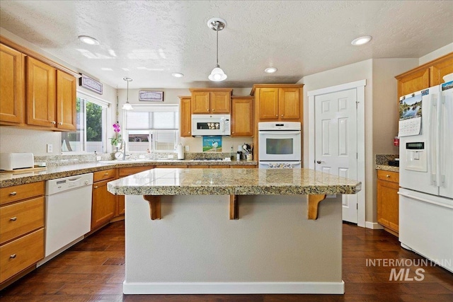 kitchen with white appliances, dark wood-style floors, a kitchen island, a breakfast bar area, and brown cabinets