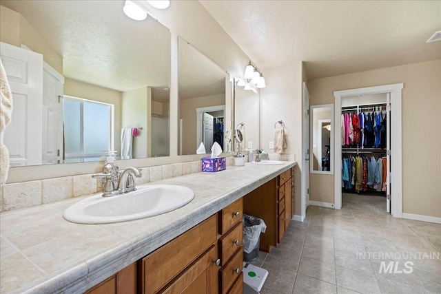 bathroom with double vanity, a walk in closet, a sink, and tile patterned floors