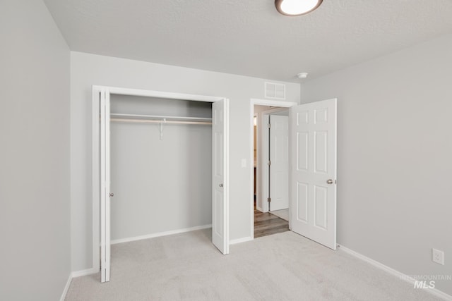 unfurnished bedroom featuring a textured ceiling, light colored carpet, and a closet