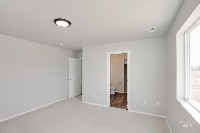 unfurnished bedroom featuring connected bathroom, light carpet, and a spacious closet