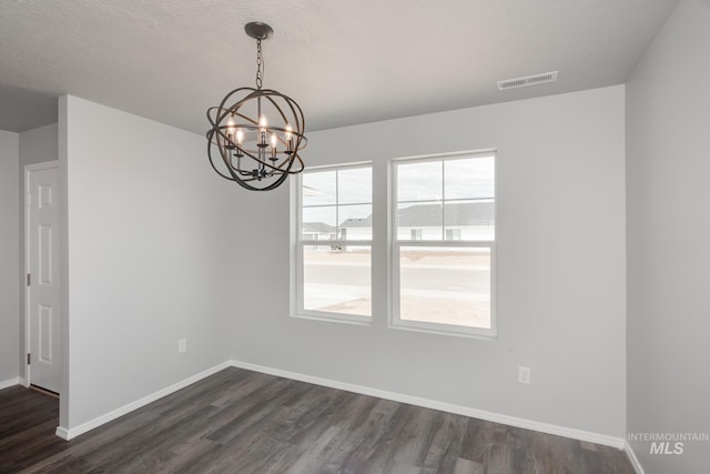 unfurnished dining area featuring a textured ceiling, dark hardwood / wood-style floors, and an inviting chandelier