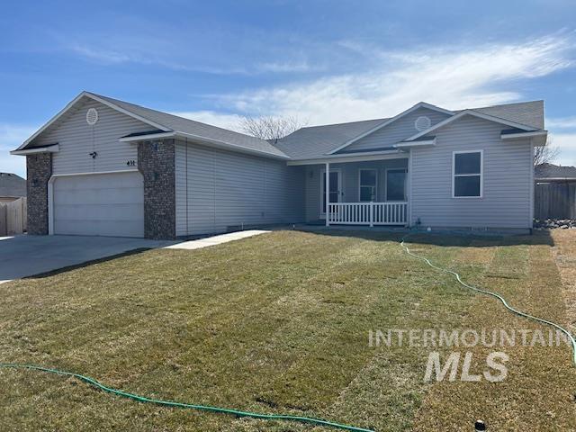 ranch-style home featuring a front yard, concrete driveway, covered porch, and a garage