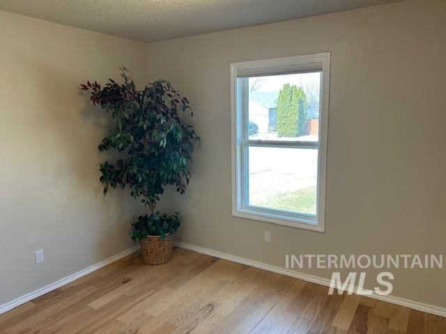 spare room with light wood-style flooring, a textured ceiling, and baseboards