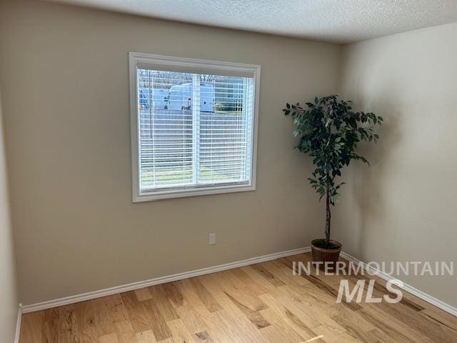 empty room featuring a textured ceiling, light wood-type flooring, and baseboards