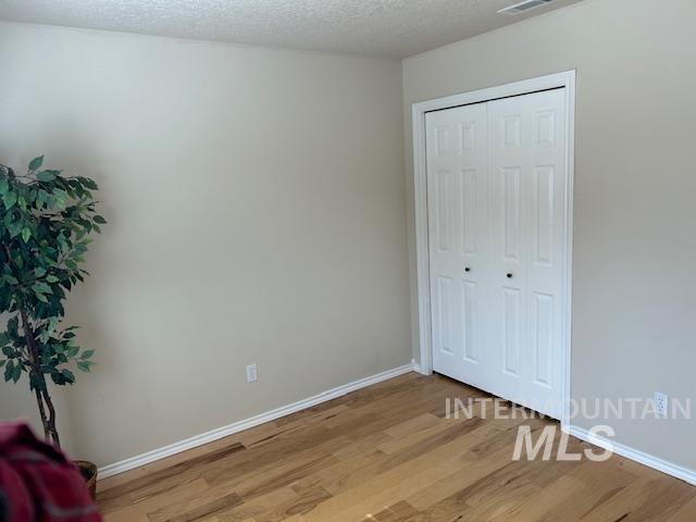 bedroom featuring baseboards, light wood-type flooring, a closet, and a textured ceiling