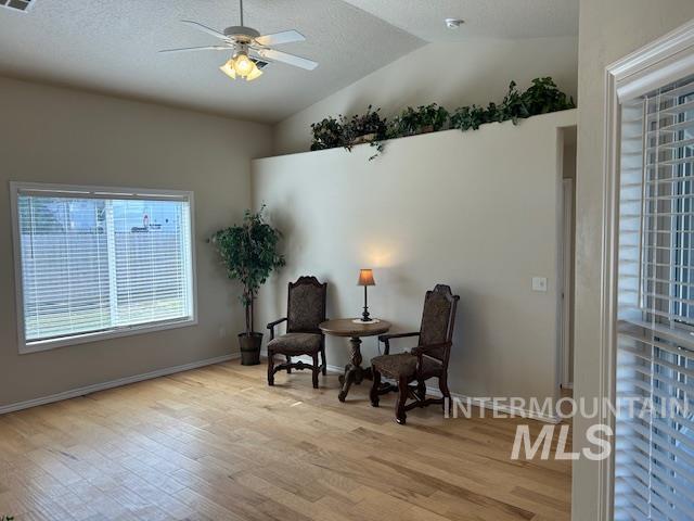 sitting room with wood finished floors, baseboards, lofted ceiling, ceiling fan, and a textured ceiling