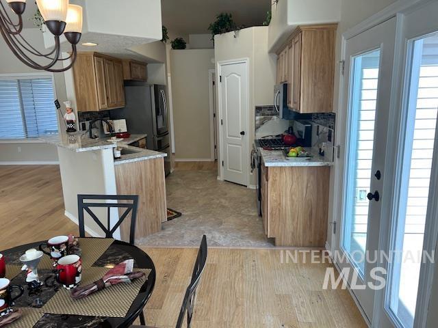 kitchen featuring stainless steel microwave, range with gas cooktop, light countertops, light wood-style flooring, and an inviting chandelier