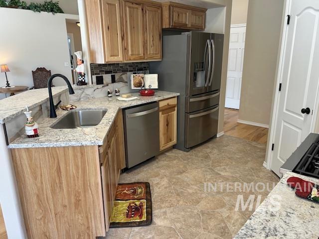 kitchen featuring a sink, appliances with stainless steel finishes, a peninsula, decorative backsplash, and light stone countertops