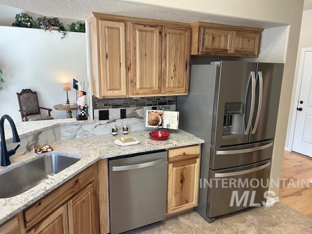 kitchen with backsplash, light stone countertops, stainless steel appliances, and a sink