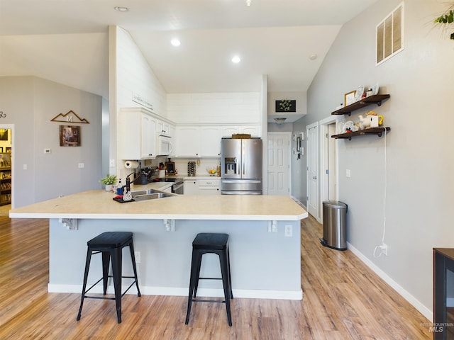 kitchen featuring a kitchen bar, stainless steel refrigerator with ice dispenser, kitchen peninsula, vaulted ceiling, and white cabinets