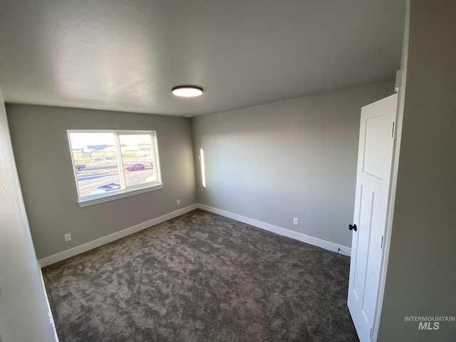 empty room featuring dark colored carpet and baseboards