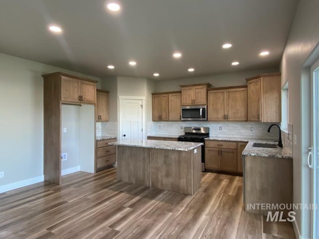 kitchen featuring a sink, light stone counters, a kitchen island, wood finished floors, and appliances with stainless steel finishes