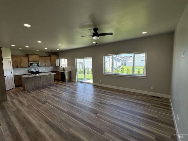 kitchen with a sink, open floor plan, stainless steel appliances, decorative backsplash, and baseboards