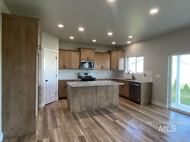 kitchen with sink, a center island, wood-type flooring, light stone countertops, and appliances with stainless steel finishes