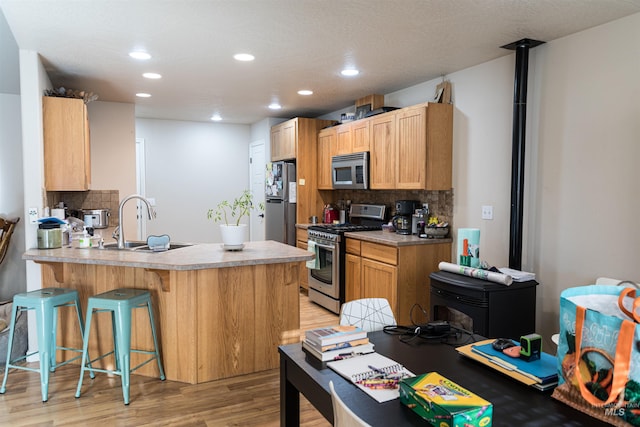 kitchen featuring kitchen peninsula, a kitchen bar, light wood-type flooring, backsplash, and appliances with stainless steel finishes