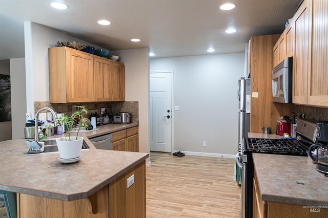 kitchen with kitchen peninsula, stainless steel appliances, light hardwood / wood-style floors, a kitchen breakfast bar, and sink