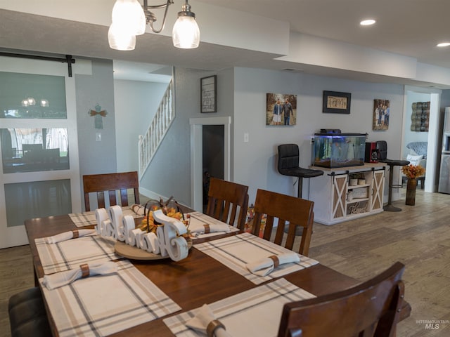 dining space with a notable chandelier, a barn door, and hardwood / wood-style floors