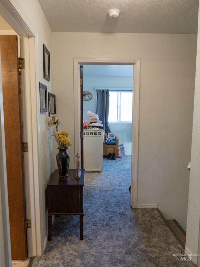 corridor featuring a textured ceiling and dark carpet