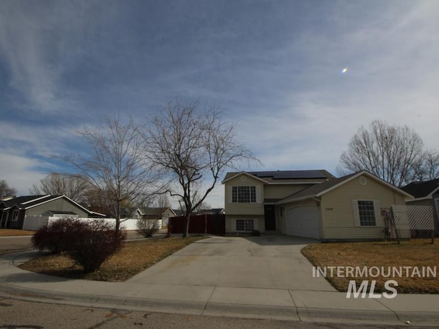 view of front of property with driveway, an attached garage, roof mounted solar panels, and fence