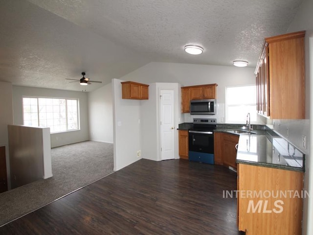 kitchen with electric stove, brown cabinets, dark countertops, stainless steel microwave, and a sink