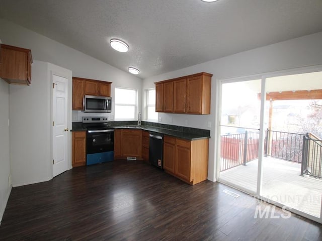 kitchen featuring lofted ceiling, range with electric cooktop, dishwasher, stainless steel microwave, and dark countertops