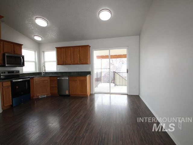 kitchen featuring lofted ceiling, stainless steel appliances, dark countertops, and a sink